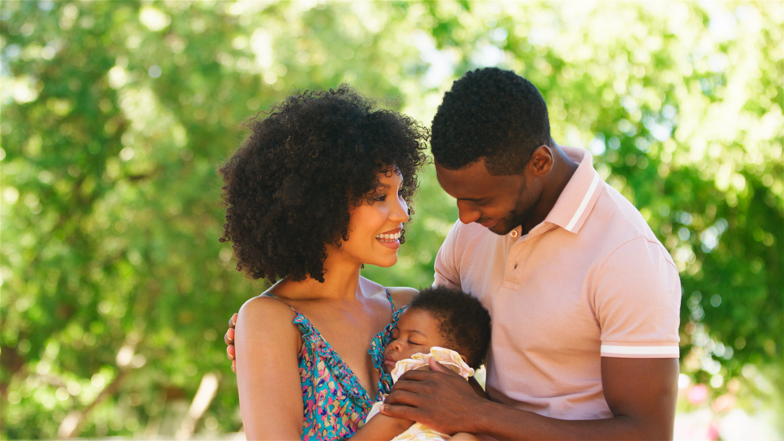 A mother and father lovingly hold their baby outdoors.