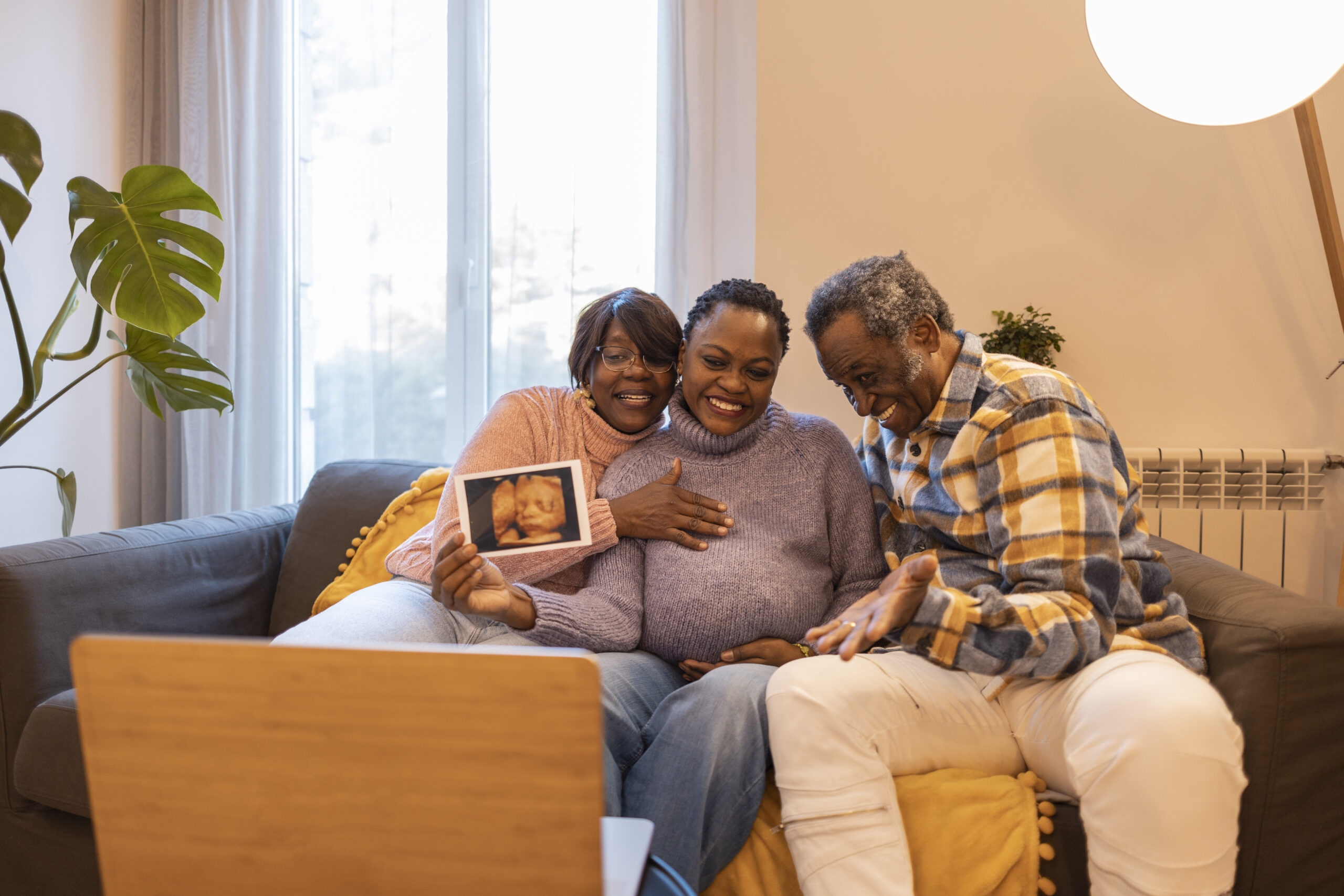 African american family of three making a video call showing ultrasound scan of pregnant daughter with a laptop
