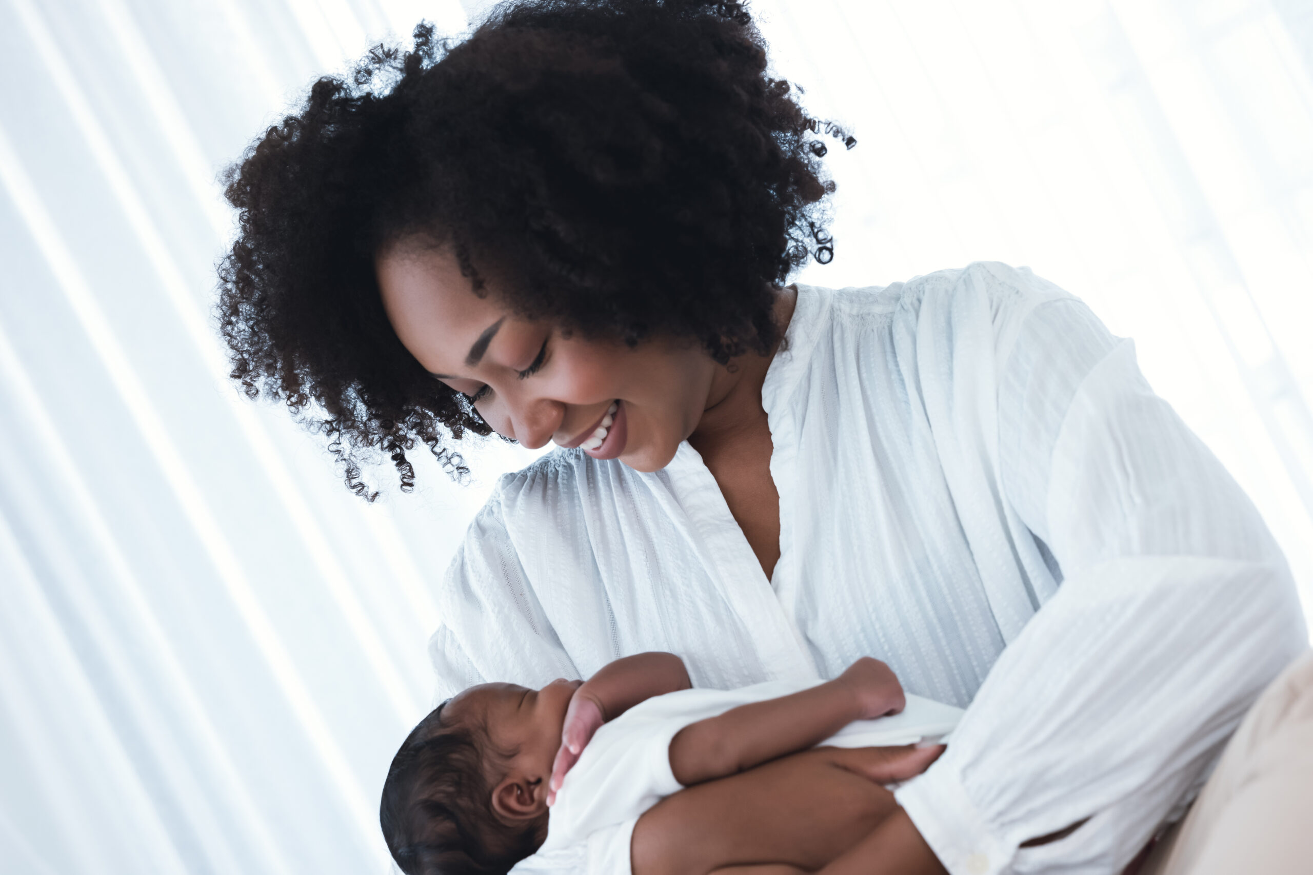 Happy African American Mother holding her newborn infant baby while sitting on bed in hospital. Mother hand lulling little child to sleeping. Child Care, Black family, Newborn baby boy. New life